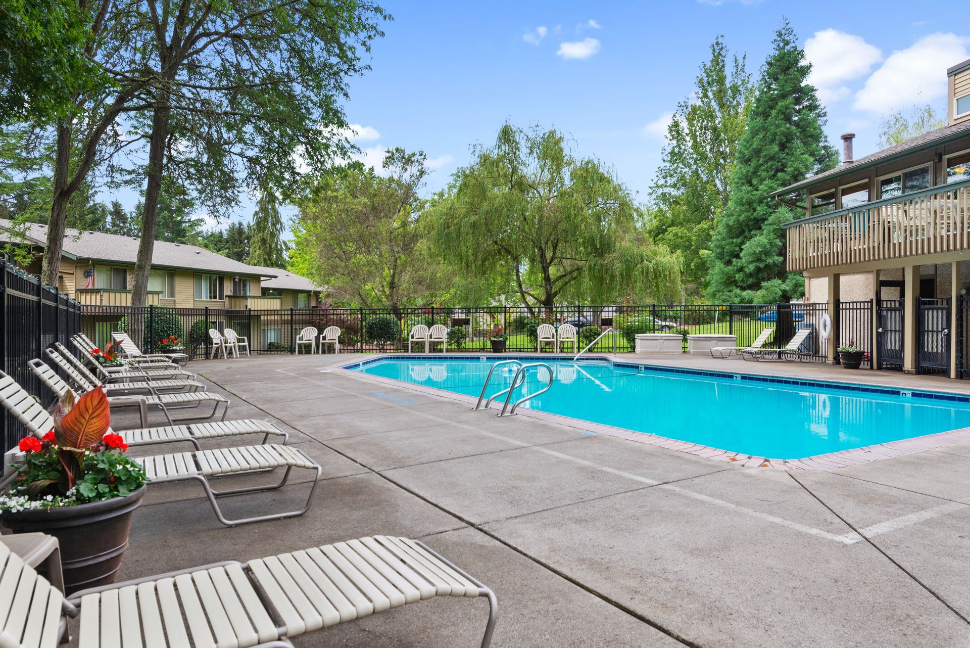 Outdoor swimming pool with lounge chairs, trees, and apartment buildings on a sunny day