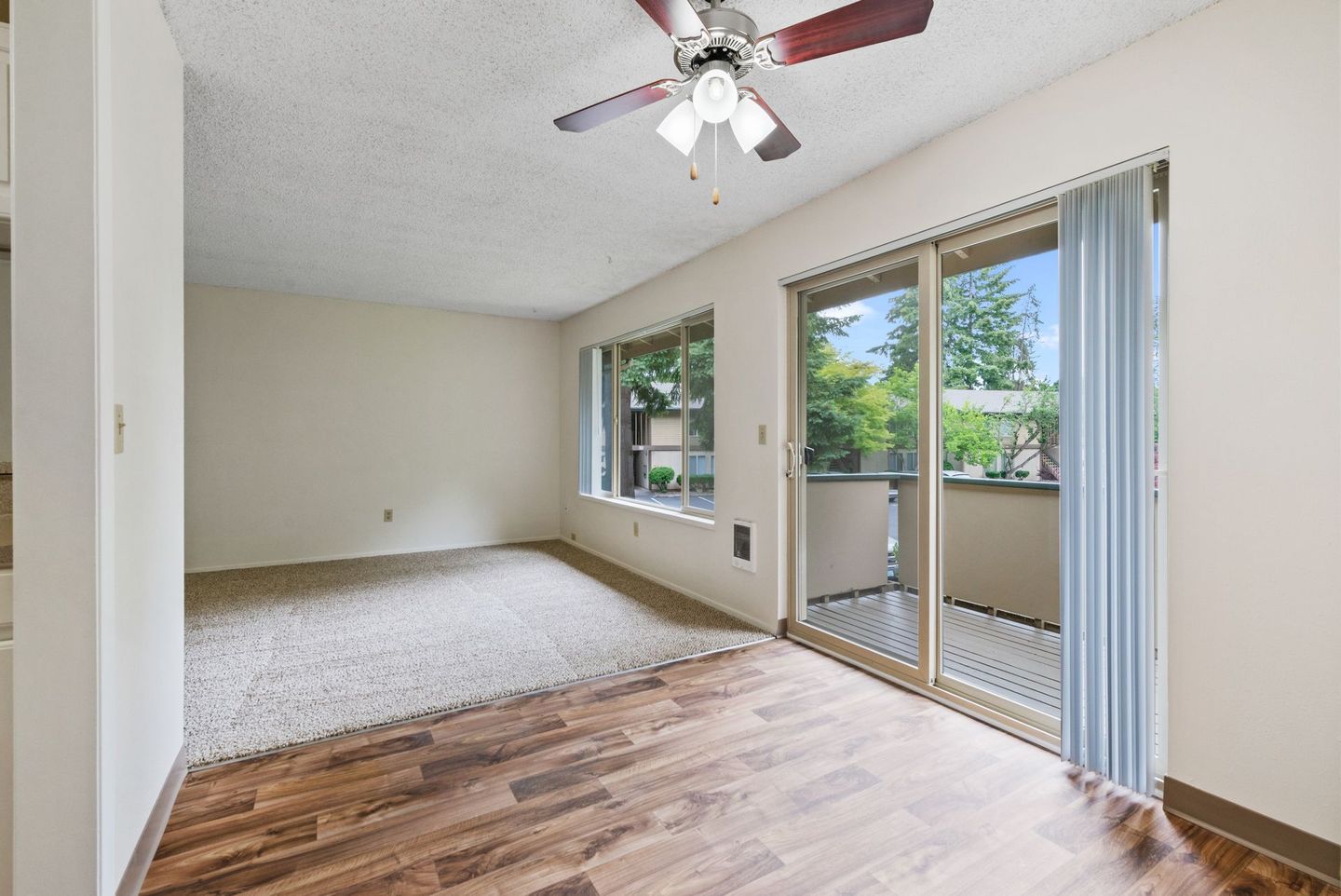 Empty carpeted bedroom with wood floor, ceiling fan, and sliding glass door to a balcony.