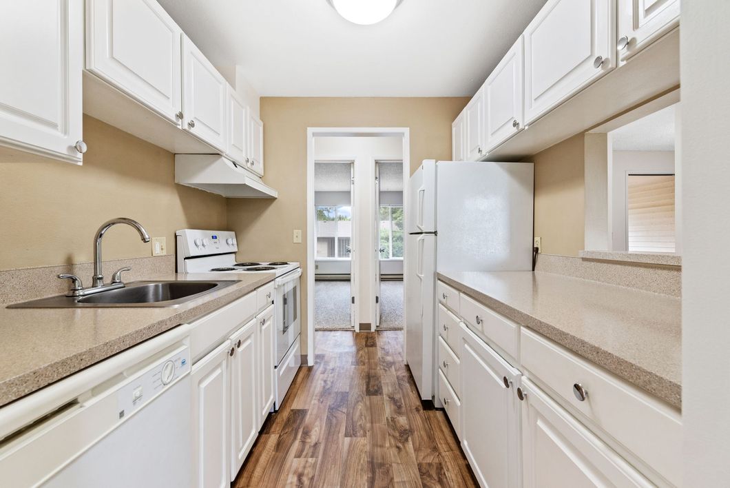 Bright white galley kitchen with white cabinets, wood floor, and stainless sink and appliances
