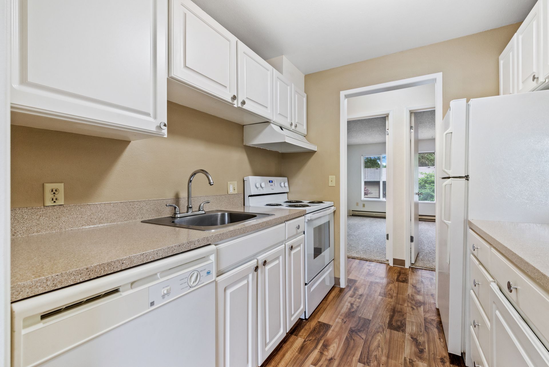 Bright white galley kitchen with cabinets, countertop, sink, and wood-look floor leading to a doorway