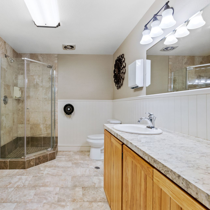 Spacious beige bathroom with glass shower, toilet, double vanity, and granite countertop.
