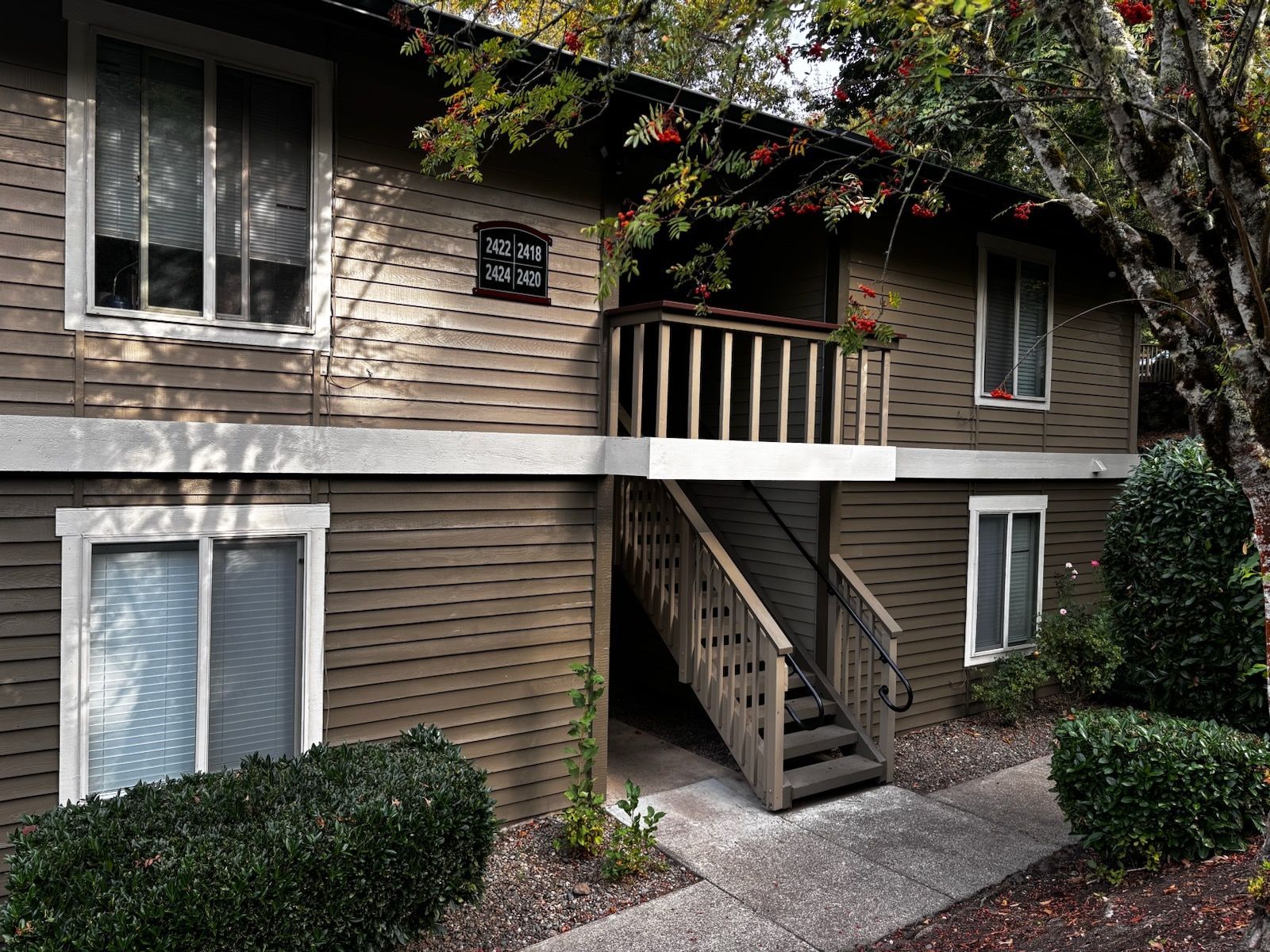 Apartment building exterior with stairs, white trim, tan siding, and shrubs in front