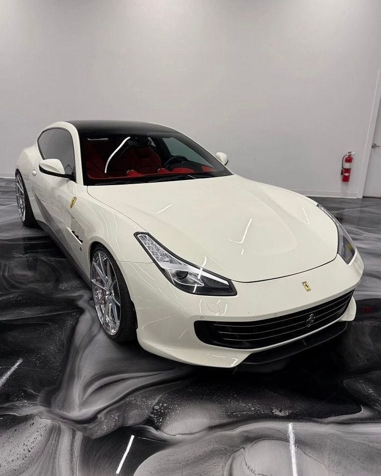 White Ferrari grand tourer on a patterned black and white floor, red interior, black roof.