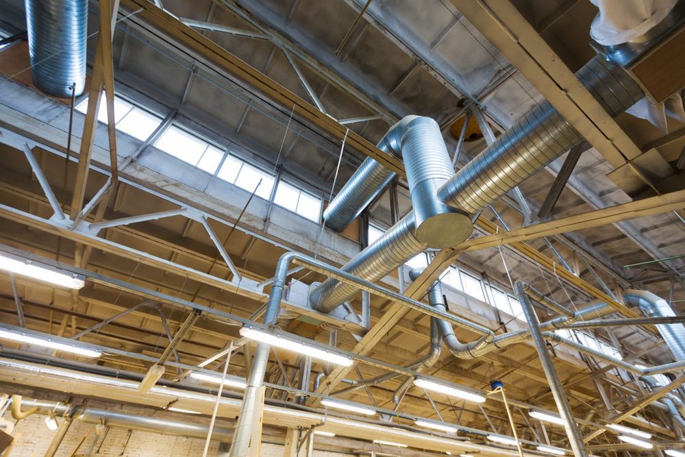 Industrial factory ceiling with metal beams, ducts, and skylights overhead