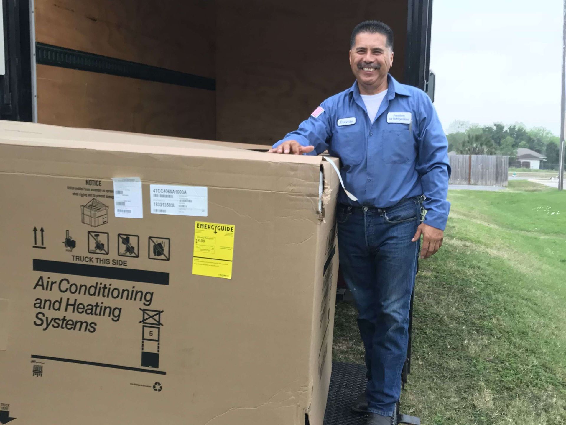 Smiling worker in blue shirt beside a large cardboard HVAC shipment outside a truck