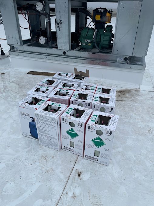 Cardboard boxes stacked on a snowy floor beside industrial equipment and a metal structure.
