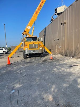 Yellow crane truck parked beside a building with traffic cones on a sunny day
