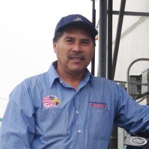 Man in a blue striped shirt and cap standing outdoors beside industrial equipment
