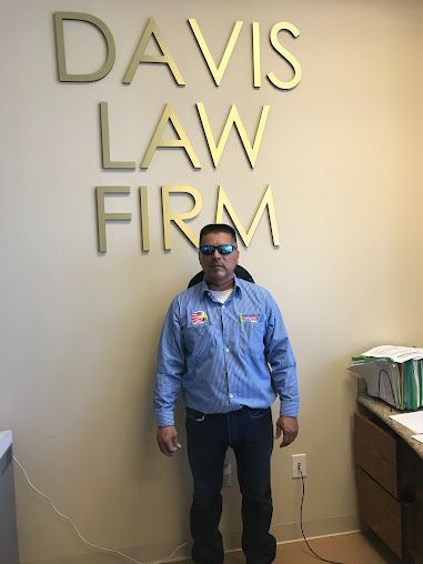 Man standing indoors in front of a wall sign reading “DAVIS LAW FIRM”