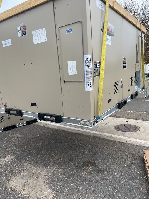 Large beige HVAC unit on a pallet beside a curb, with yellow straps and wet pavement nearby.