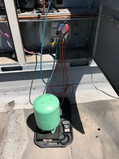 Green HVAC refrigerant tank on a scale, with hoses attached to an outdoor service unit.