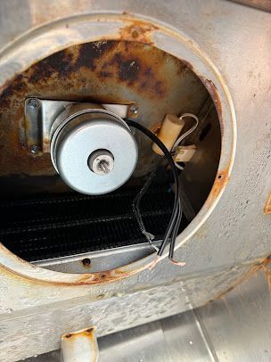 Rusted metal vent housing with a small motor and wiring inside the opening