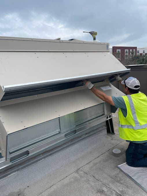 Worker in neon safety vest adjusts a rooftop vent on a white building