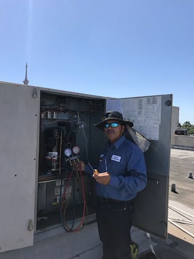 Technician in blue jacket inspects an open electrical cabinet outdoors under a clear sky.