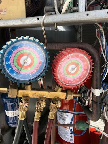 Two HVAC manifold gauges, blue and red, connected to refrigeration lines with hoses and valves.
