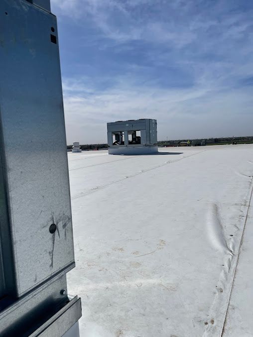 Snow-covered rooftop with a small utility structure under a cloudy sky, viewed beside a metal wall.
