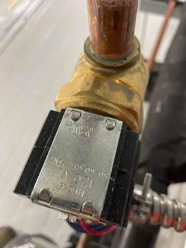 Close-up of a brass valve with a black solenoid coil and copper pipe connection