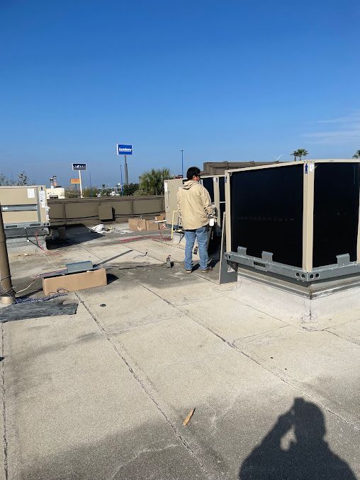 Person standing on a rooftop beside large HVAC units under a clear blue sky.