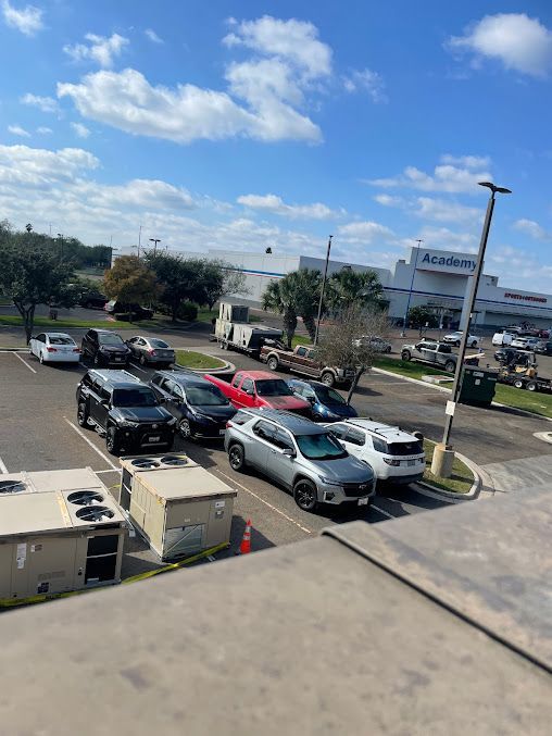 Parking lot with several cars under a bright blue sky, viewed from an elevated building.