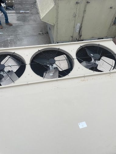 Three rooftop HVAC fans in a white unit beside a concrete wall, with one fan covered in plastic.