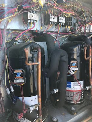 Open refrigerator compressor compartment with exposed wiring and three black compressors inside.