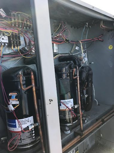 Open HVAC cabinet with two black compressor units and exposed wiring inside.