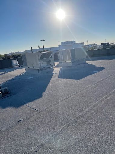 Sunny rooftop with white HVAC units and long shadows on a flat gray roof