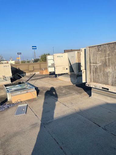 Rooftop utility area with HVAC units, cardboard boxes, and a long shadow cast on the pavement under a clear blue sky