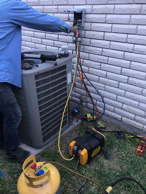 Technician servicing outdoor HVAC unit with gauges and hoses beside a house wall