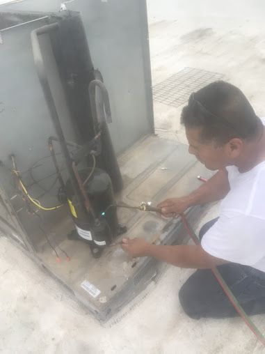 Technician kneeling beside HVAC unit, using tools to connect or repair wiring on a rooftop platform