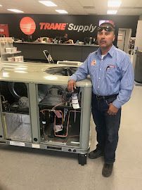 Man standing beside a large HVAC unit inside a Trane Supply showroom.