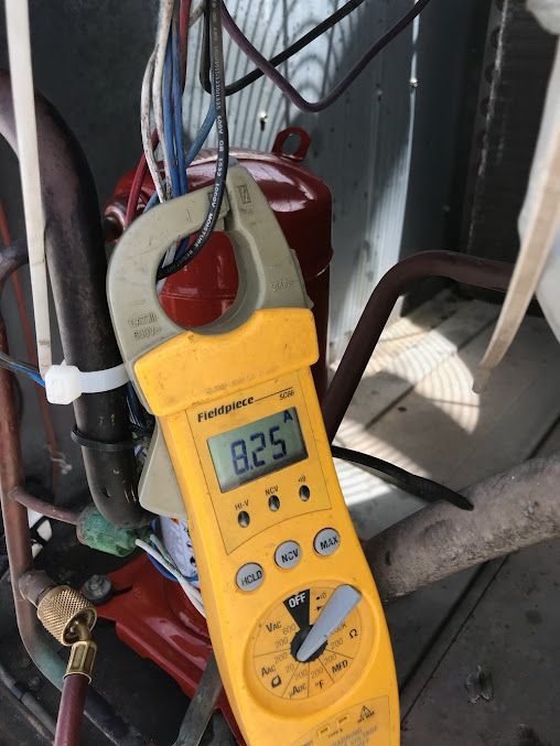 Yellow clamp meter reading 8.29 on red HVAC equipment with wires attached