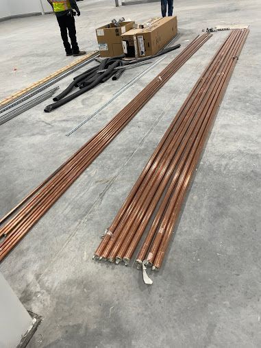 Bundles of copper pipes and metal rods laid on a concrete floor in an industrial warehouse.