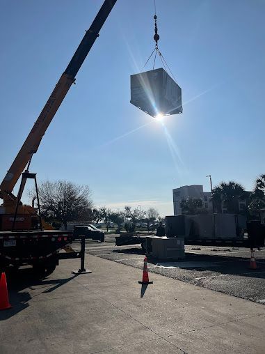 Crane lifting a large metal container over a sunlit construction site with traffic cones.