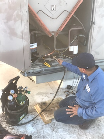 Technician in blue uniform inspecting machinery beside a black gas cylinder outdoors