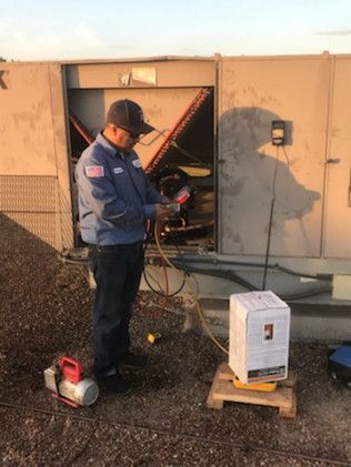 Technician inspecting rooftop HVAC unit with tools beside it on a gravel surface