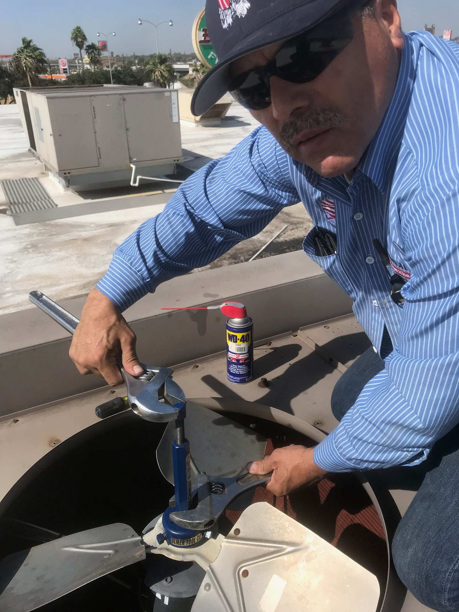 Man on a rooftop using a wrench to adjust outdoor HVAC equipment beside a spray can