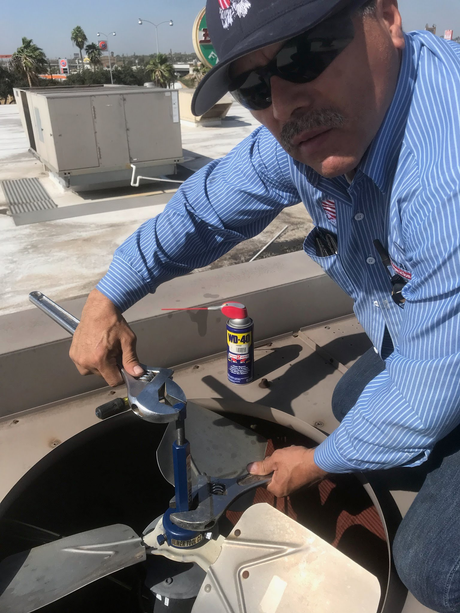 Worker in blue shirt and cap adjusting rooftop HVAC unit with a wrench.