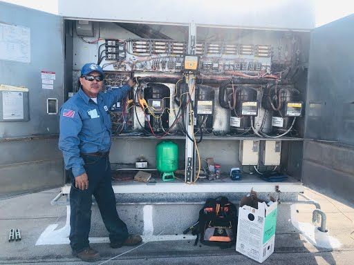 Technician standing beside an open electrical panel outdoors, with tools and equipment on the ground.