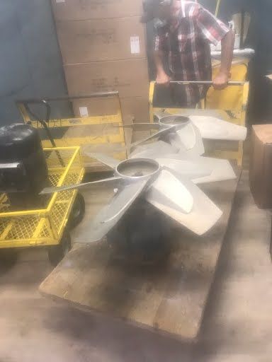 Workshop table with several white fan blades and metal parts, with yellow crates in the background