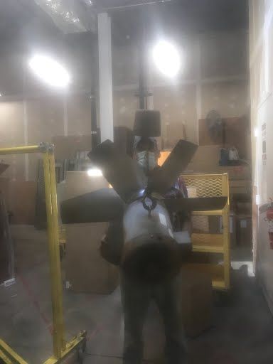 Person in a warehouse wearing a backpack sprayer near yellow safety railings and machinery