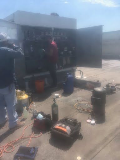 Workers using tools beside an open truck in a sunlit parking lot