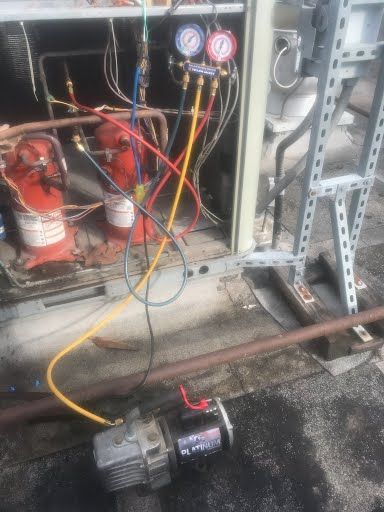 Industrial equipment with red compressor, gauges, hoses, and a motor on a wet floor in a utility area
