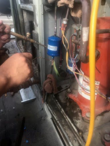 Hands working on industrial machinery with pipes, wires, and a blue filter inside a metal compartment
