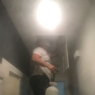 Person in a white shirt using a paint sprayer near a ceiling light indoors