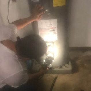 Person inspecting a lit wall-mounted electrical unit with another person standing nearby in a dim room