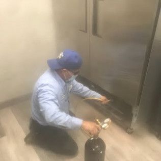 Person kneeling beside a stainless-steel machine, spraying or cleaning the lower area with a hose.