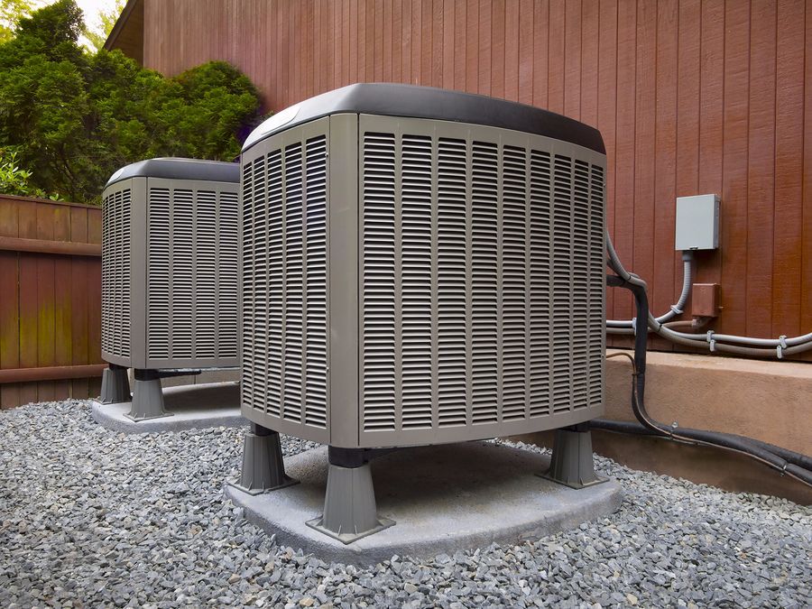 Two outdoor HVAC units on gravel beside a wooden building