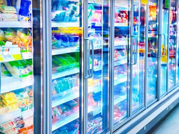 Supermarket freezer aisle with rows of glass-door refrigerators and colorful packaged frozen foods