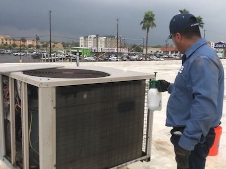 Worker inspecting a large rooftop HVAC unit on a building roof near the waterfront